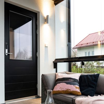 Moderner Wintergarten mit energieeffizienter LED-Beleuchtung, schwarzer Tür, grauem Sofa mit bunten Kissen, Glaswänden, die das Haus mit einem leuchtend roten Dach präsentieren.