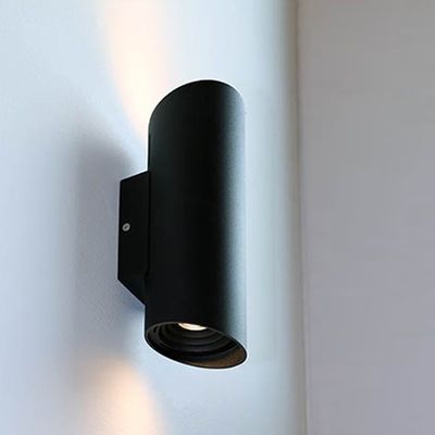 Moderne schwarze zylindrische Wandleuchte mit weißer Wand. Das bidirektionale LED-Licht strahlt nach oben und unten für eine elegante Beleuchtung.