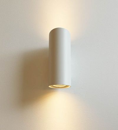 Eine stilvolle, zylindrische LED-Wandleuchte, die warme Lichtstrahlen an einer weißen Wand nach oben und unten wirft; ideal für moderne, minimalistische Innenräume.