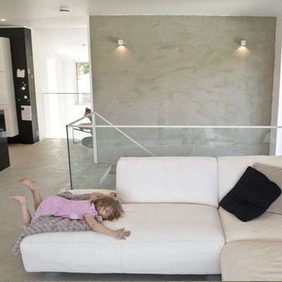 Ein Kind in einem rosa Kleid auf einem weißen Sofa in einem modernen Wohnzimmer mit minimalistischem Dekor und energieeffizienter LED-Beleuchtung.