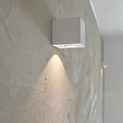 Eine minimalistische, quadratische LED-Wandleuchte, die ein warmes Licht auf einer strukturierten grauen Wand für eine moderne Innenbeleuchtung erzeugt.