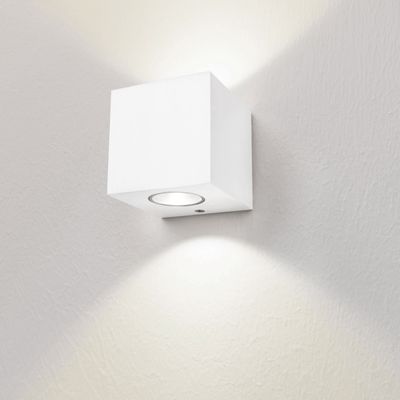 Eine minimalistische weiße Würfelwandleuchte beleuchtet eine sanft strukturierte weiße Wand mit nach oben und unten gerichtetem Licht. Perfekt für moderne LED-Beleuchtung.