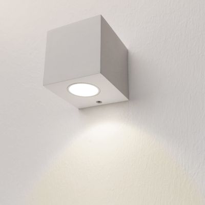 Alternativer Text: Würfelförmige LED-Wandleuchte strahlt weiches weißes Licht auf eine strukturierte Wand, ein modernes Beleuchtungsdesign für Ihr Zuhause oder Büro.