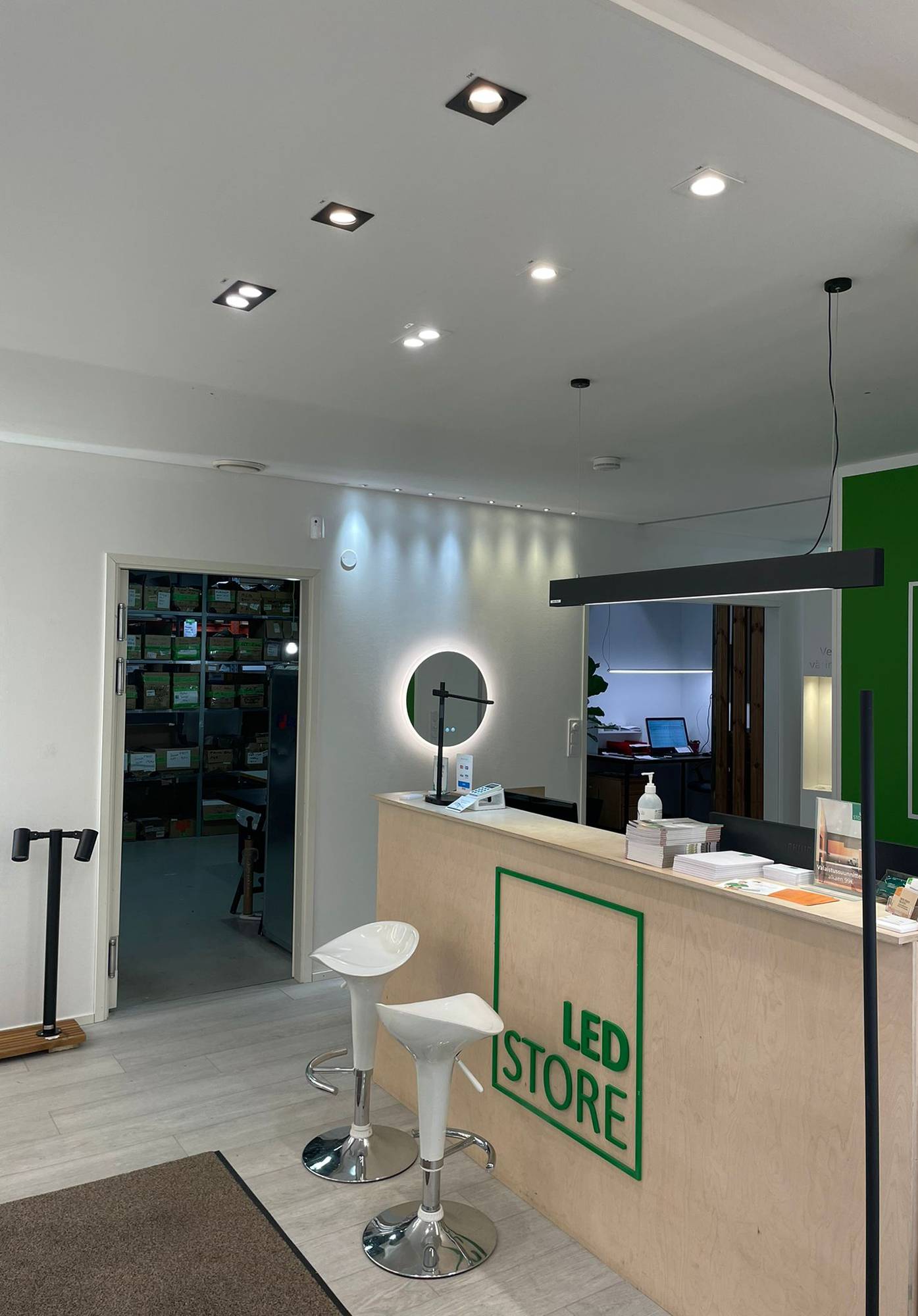 Led-Leuchten im Ausstellungsraum von Ledstore. Spots an der Decke vor der Theke und eine VIIVA-Deckenleuchte über der Theke. Die Wand ist mit 3W-Spots akzentuiert, fest und gerichtet. Moon 600 Lichtspiegel unter den Spots. Ledstore.fi