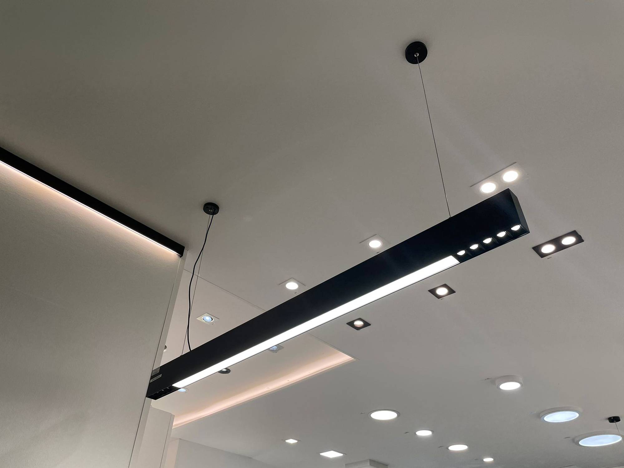 Ledstorella Viiva-Leuchte über der Verkaufstheke. Led-Leiste auf einem Ersatz-Aluminiumprofil in der Decke für indirektes Licht sowie Spotlights und Panel-Leuchten an der Decke. Ledstore.fi