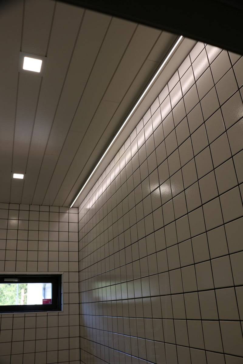 Wohnungsmesse 2019: Led-Leiste an der Decke neben der Wand, Licht wird von der glänzenden Fliese reflektiert. Ledstore.fi