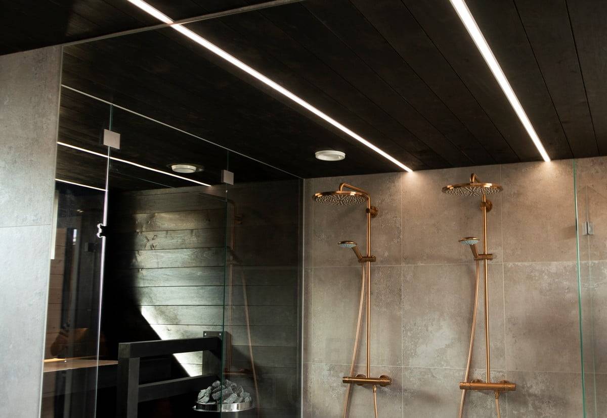 Wohnmesse 2020: LED-Leisten beleuchten das Badezimmer in schmalen Einbauprofilen in der schwarzen Decke des Waschraums. Die Lichtlinien erhellen den Raum mit hochwertigem und angenehmem Licht. Ledstore.fi
