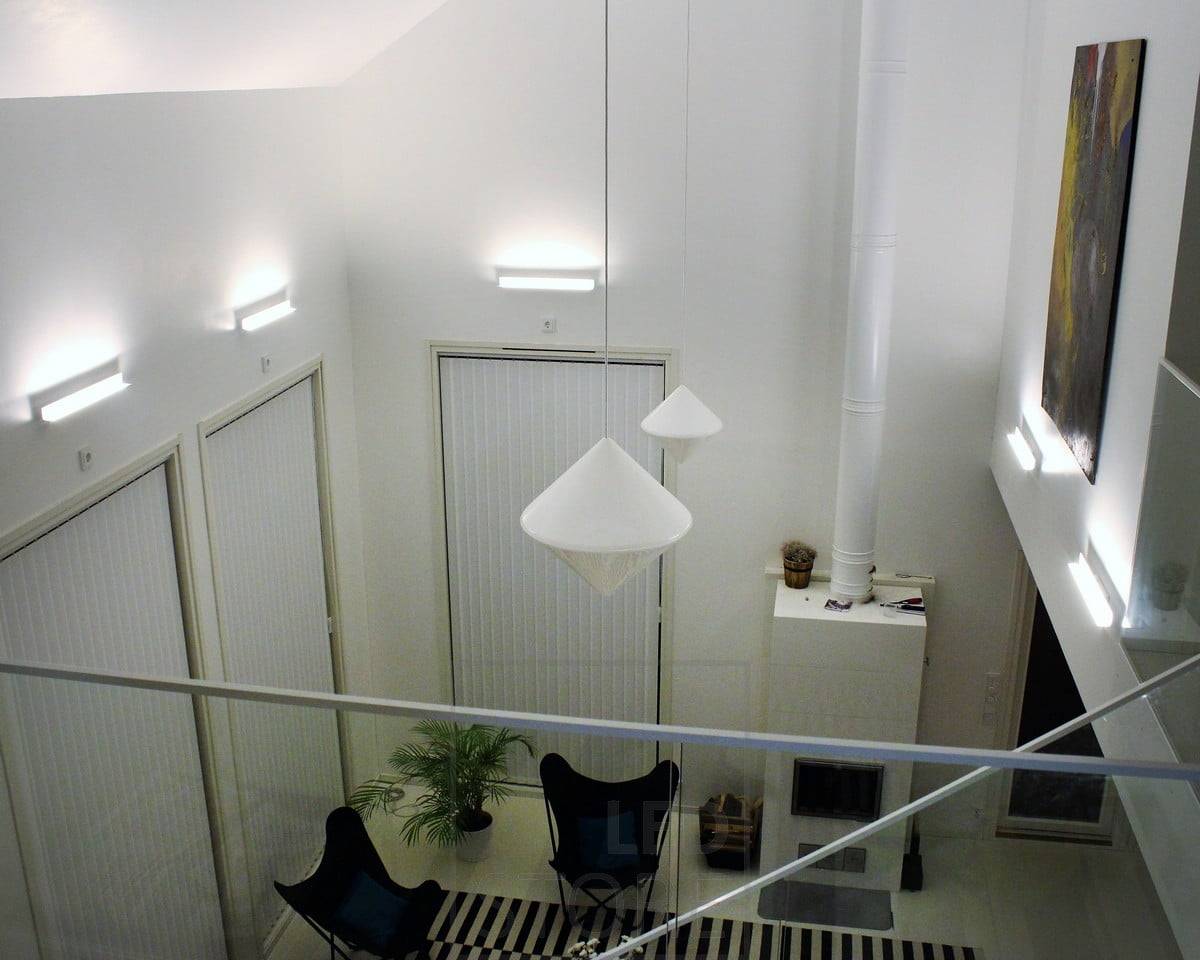 Ein Wohnzimmer mit stimmungsvoller indirekter Beleuchtung, die mit Led BLADE Wandleuchten erzeugt wurde. Die Leuchte ist so montiert, dass sie von unten nach oben leuchtet. So betont die indirekte Beleuchtung auch die Höhe des Raums und die Kunstwerke an der Wand. Ledstore.fi