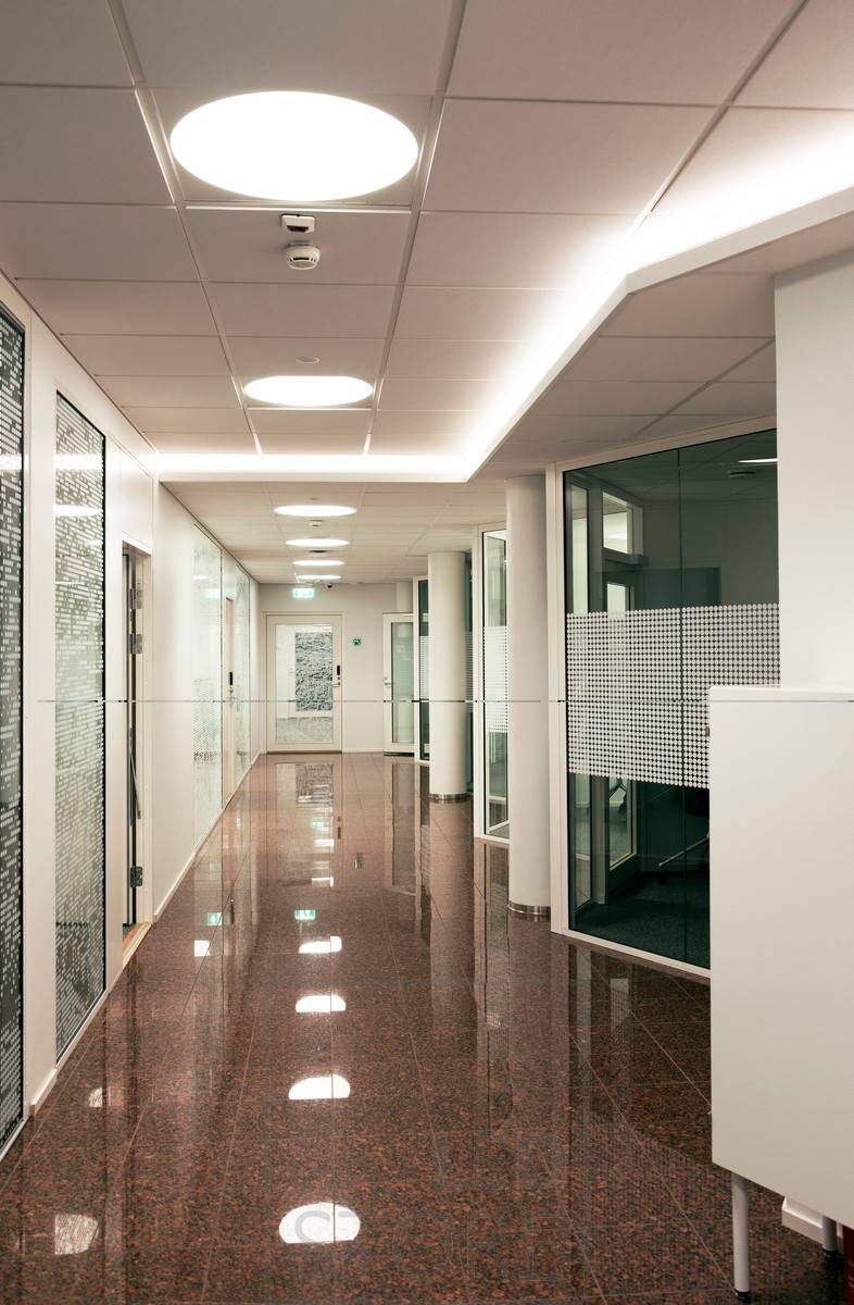 Am Downlight eines Korridors montierte Led-Leiste, die stimmungsvolles indirektes Licht durch die Decke erzeugt. Allgemeinbeleuchtung mit Plafondi-Einbauleuchten.
