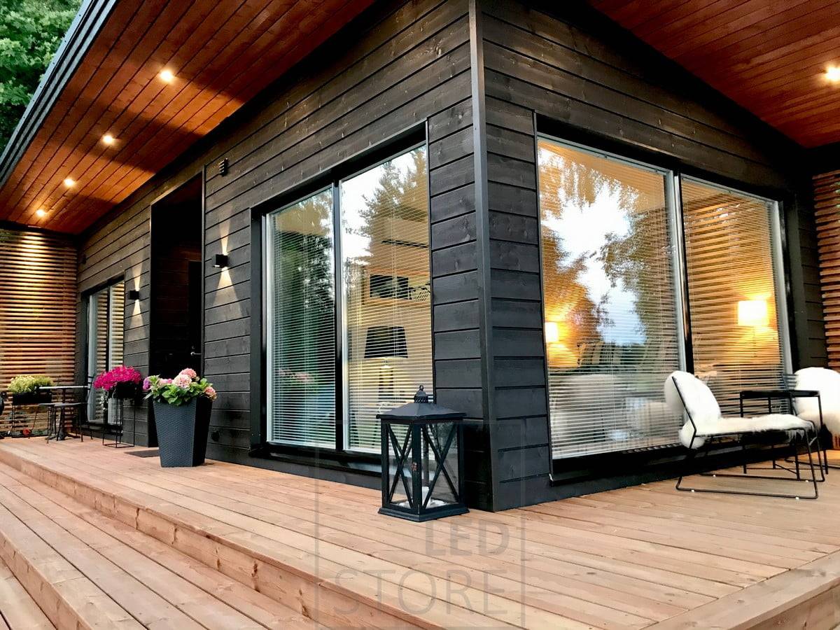 Schwarze FUNK LED-Wandleuchten, die die Fassade des Gebäudes hervorheben und indirektes Licht spenden. Schwarze KANTTI Richtstrahler auf dem Terrassendach. LINJA5-Leuchten zur Akzentuierung der Verkleidung. Ledstore.fi