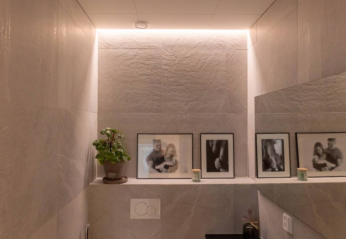 Zwischen Wand und Decke in einem Toilettenraum bündig montierte LED-Leiste.