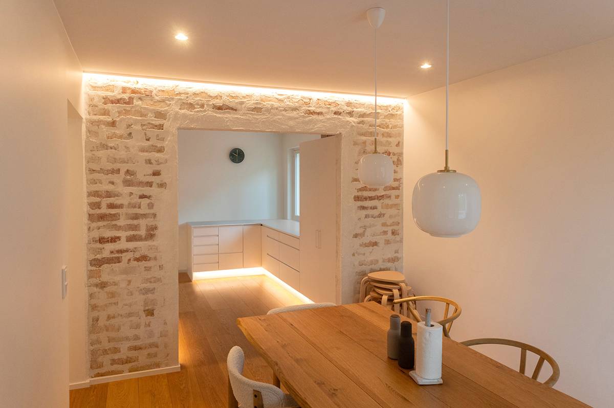 An den Sockelleisten der Küche ist ein LED-Streifen angebracht, der den Bodenrand beleuchtet. Auf der Seite des Essbereichs beleuchtet ein LED-Streifen am oberen Rand der Akzentwand die Wand nach unten hin. Außerdem befinden sich an der Decke Strahler und Hängeleuchten.