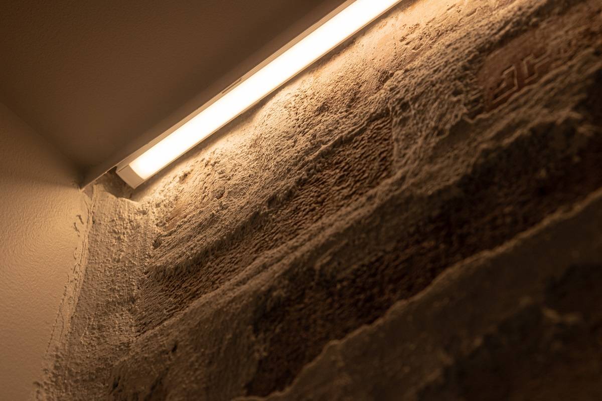 Nahaufnahme der Montage eines LED-Streifens an einer Akzentwand. Der LED-Streifen wurde in einem auf der Oberfläche montierten Aluminiumprofil zwischen der Leiste und der Wand angebracht.