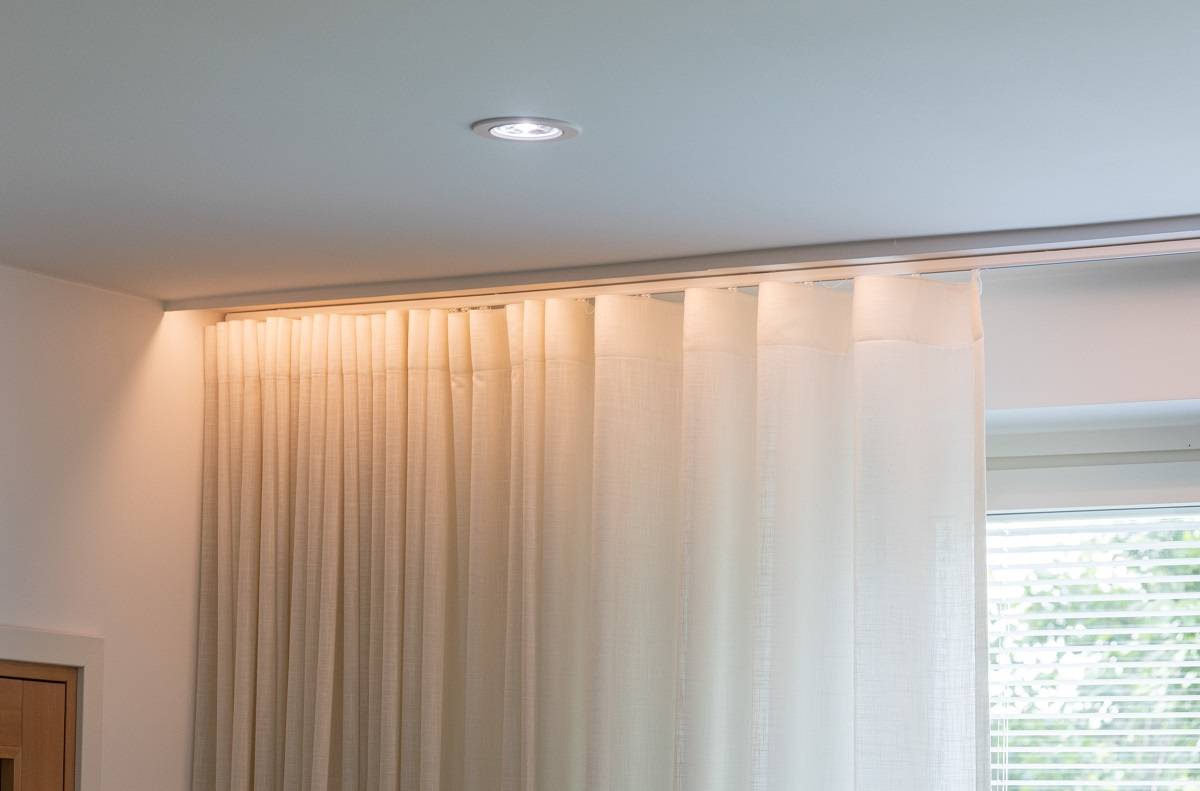 Downlight an der Decke des Wohnzimmers. Vor dem Vorhang ist ein LED-Streifen hinter der Leiste angebracht, sodass die Lichtquelle verborgen bleibt.
