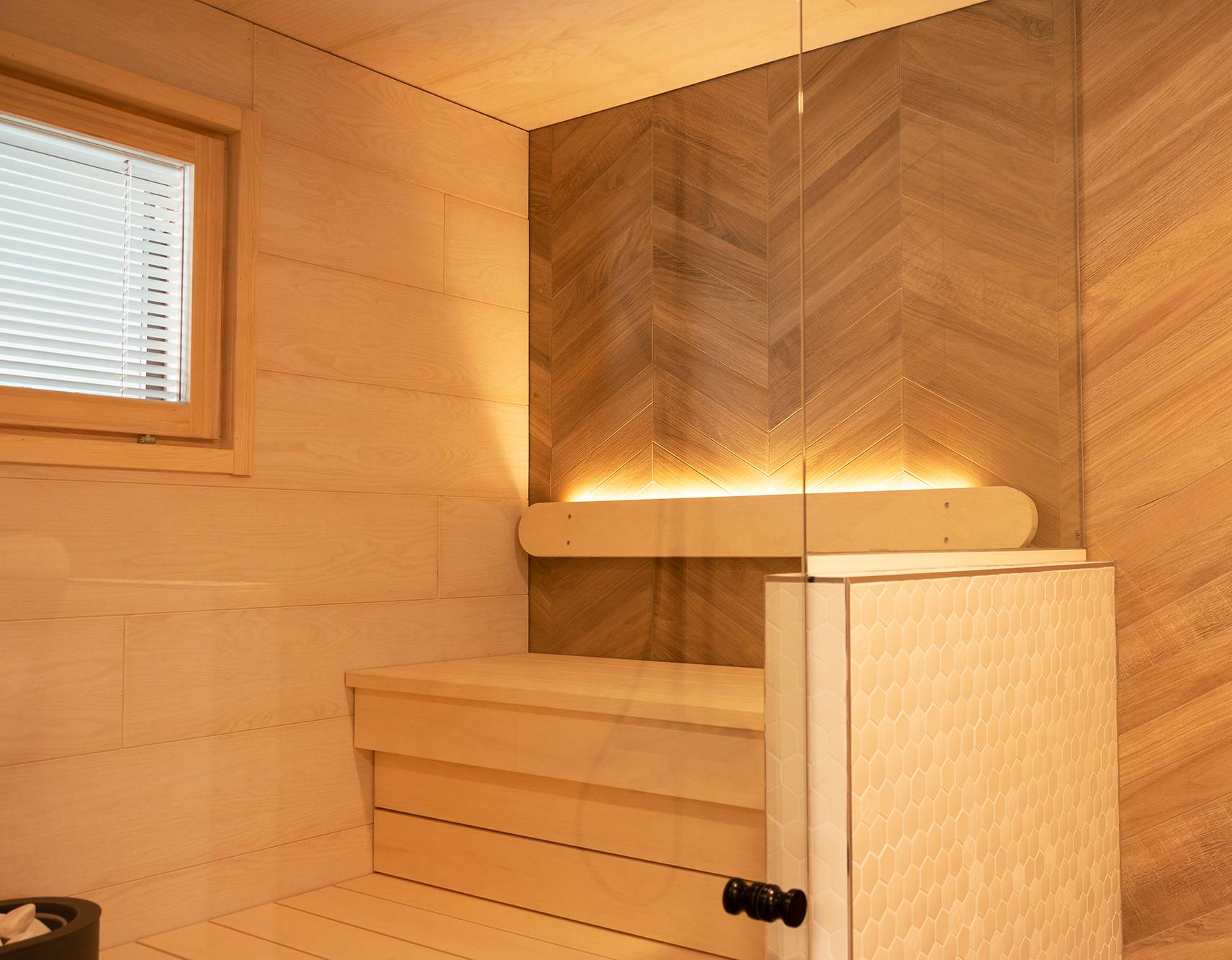 Die Beleuchtung der Sauna wurde mit einer nach oben gerichteten LED-Leiste an der Rückenlehne realisiert. Die Beleuchtung im Waschraum erhellt dank der Glaswände auch die Sauna. Ledstore.fi