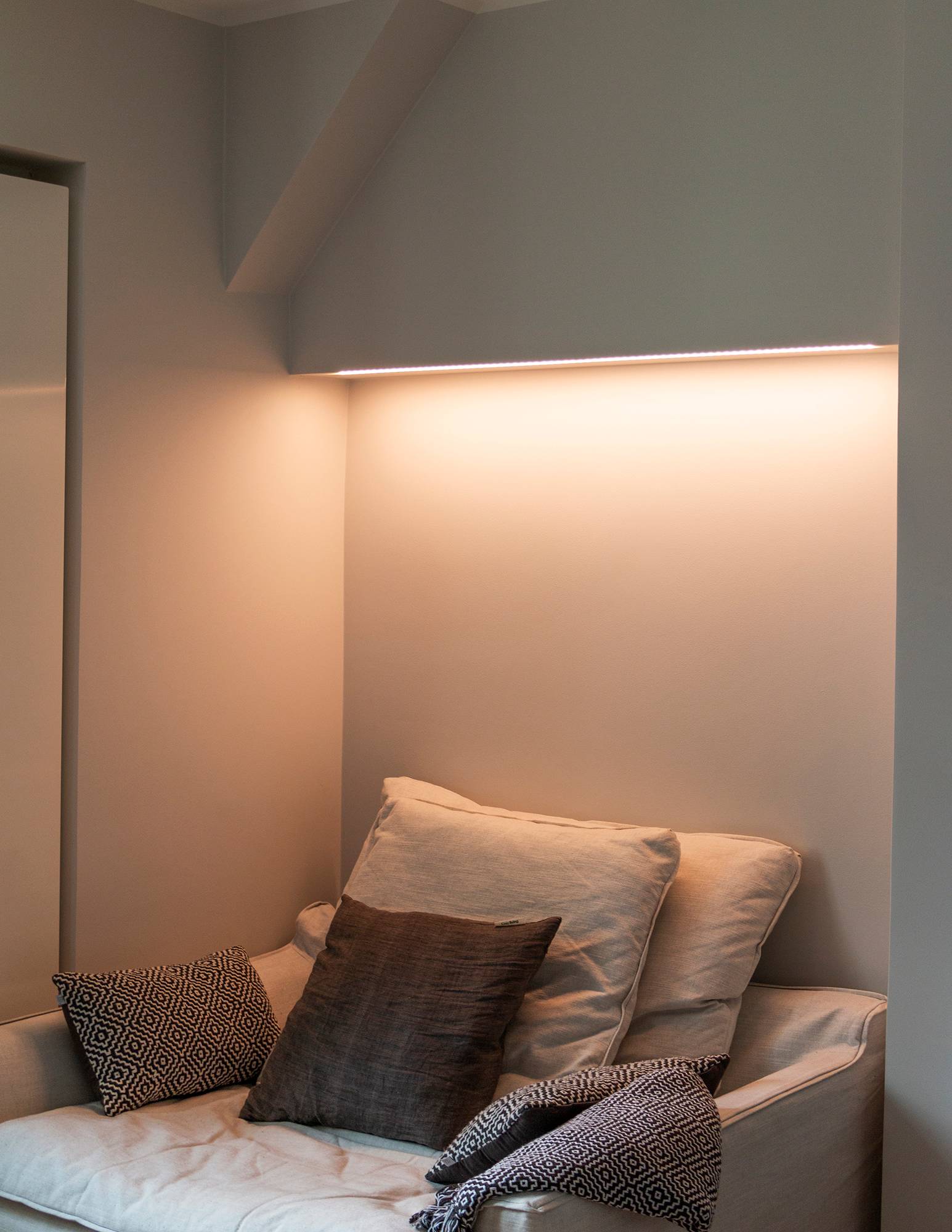 Schlafzimmer mit in der Farbtemperatur einstellbarer Stimmungsbeleuchtung über dem Bett, LED-Leiste an der Unterseite des Schranks in einer flachen Oberfläche montiert. Das Licht hat auf dem Bild einen warmen Ton. Ledstore.fi