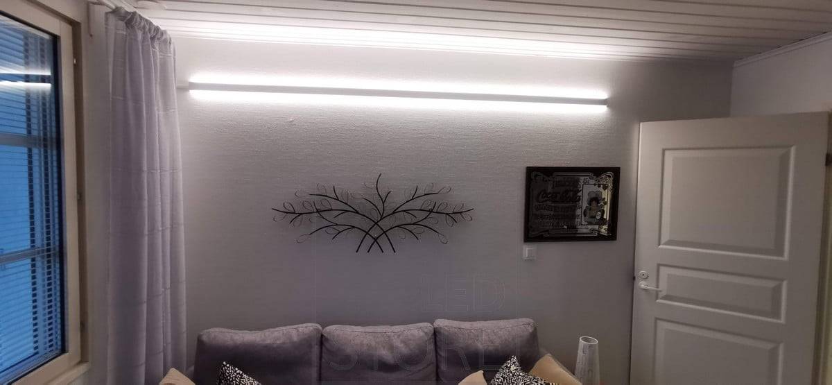 Hinter dem Sofa, an der Wand, ein bidirektionales LED-Profil. Zwei LED-Streifen auf dem Profil. Ledstore.fi