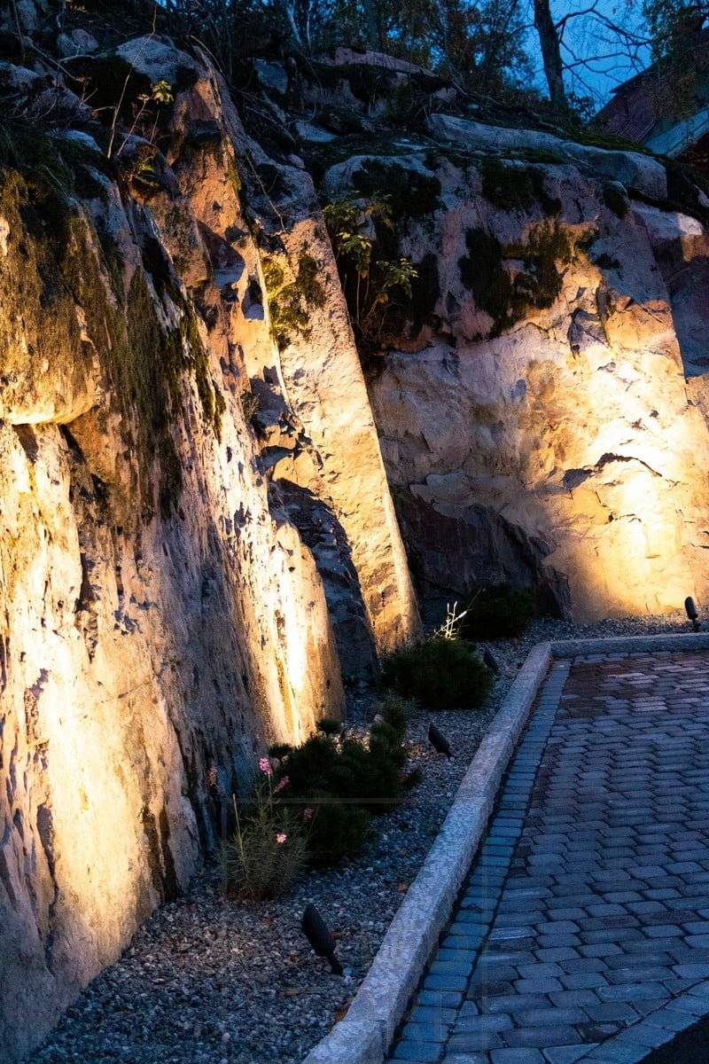 Led SPIKE Bodenleuchte, die den Felsen beleuchtet und hervorhebt. Das Gehäuse der Leuchte ist mattschwarz und hat einen Neigungswinkel von 40 Grad. Ledstore.fi