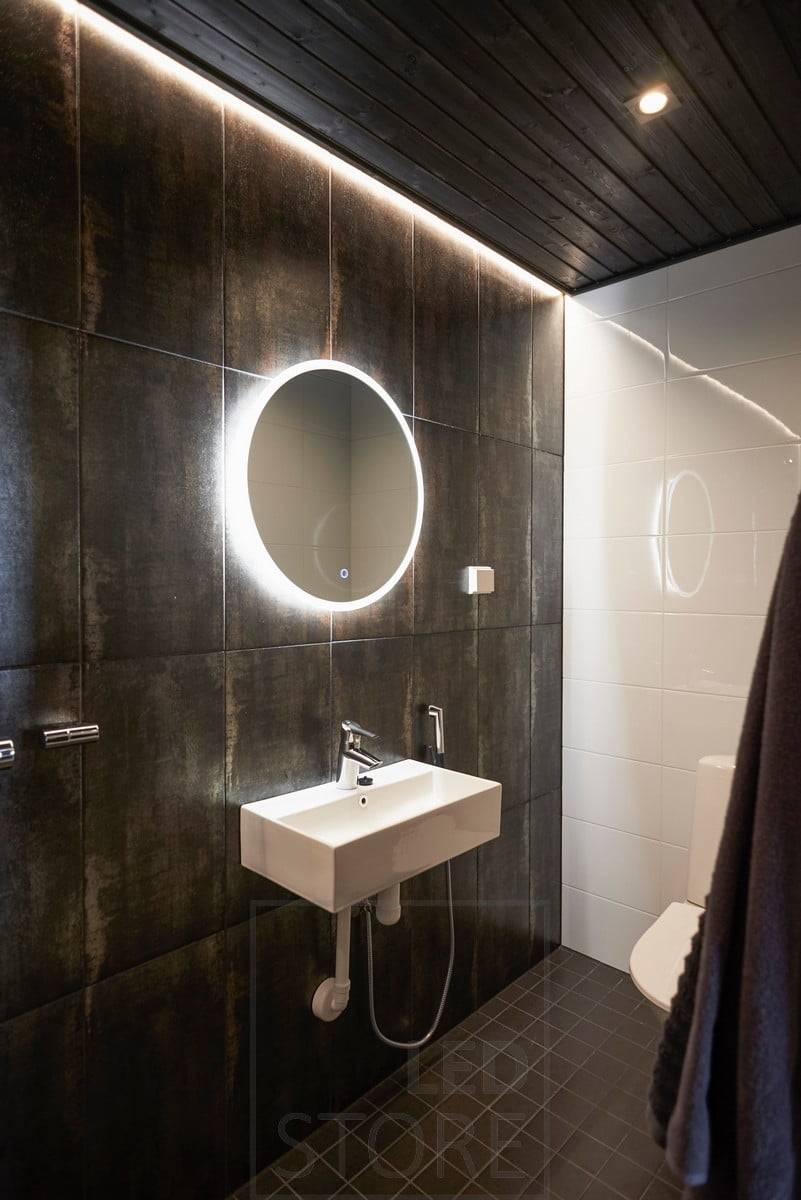 Dunkles Badezimmer, das mit Spotlighting und indirektem Licht stimmungsvoll beleuchtet wird. Der Lichtspiegel verfügt über eine Entfogging-Funktion, die den Spiegel hell hält, wenn man aus der Sauna oder Dusche kommt. Ledstore.fi