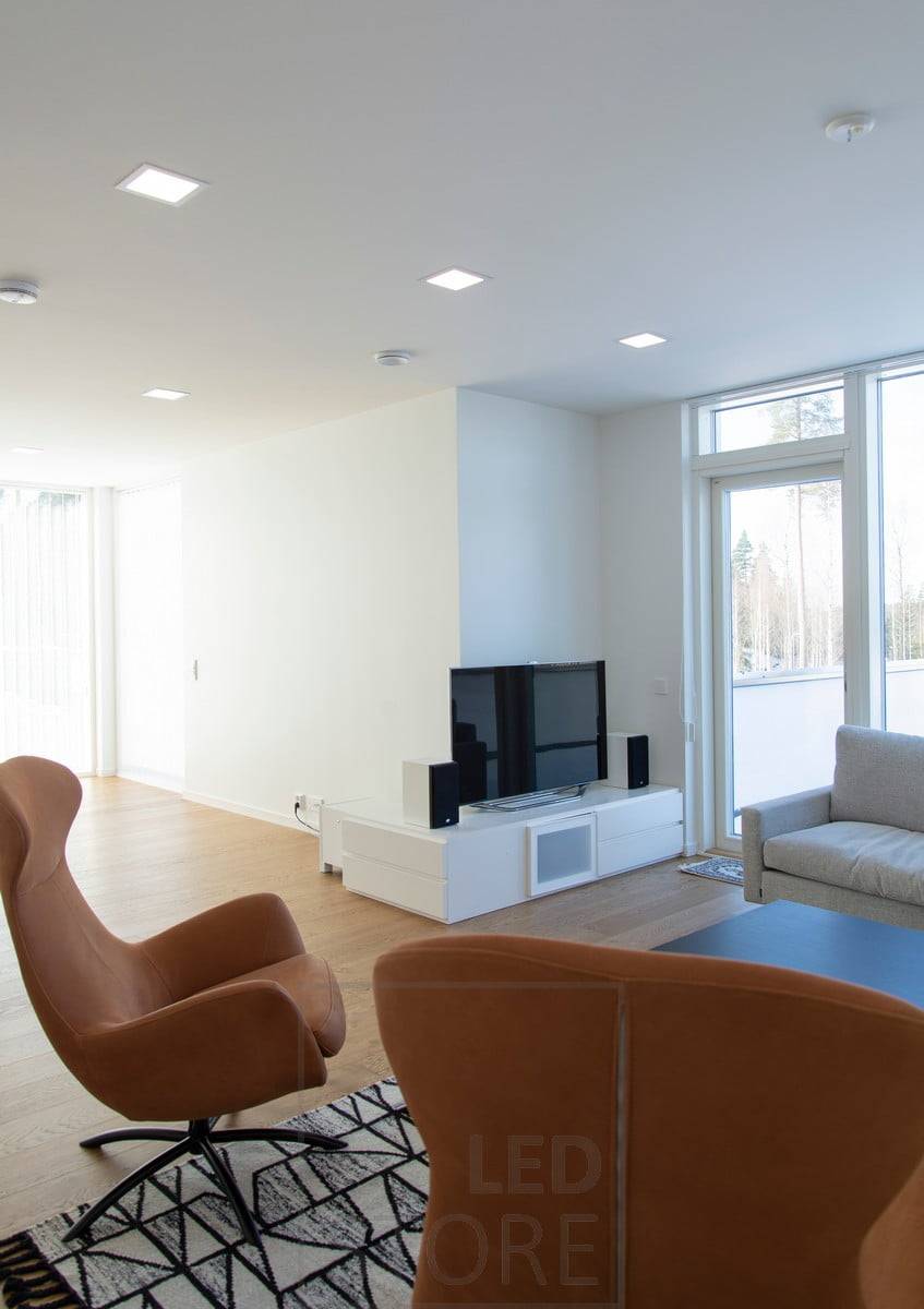 Minimalistische Paneelleuchten fügen sich harmonisch in die weiße Decke ein und leuchten das Wohnzimmer gleichmäßig aus. Die moderne Designsprache passt gut zum skandinavischen Interieur. Ledstore.fi