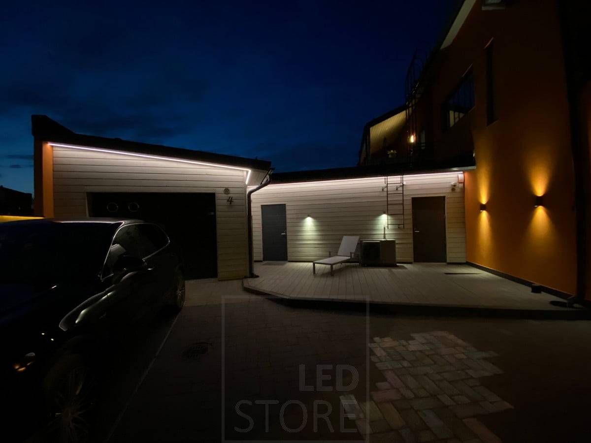 Led-Leiste an der Traufe, die die Fassade einer Garage und einer Lagerhalle mit indirektem Licht beleuchtet. Zusätzlich zur Traufbeleuchtung beleuchten Wandleuchten in eine und zwei Richtungen. Ledstore.fi