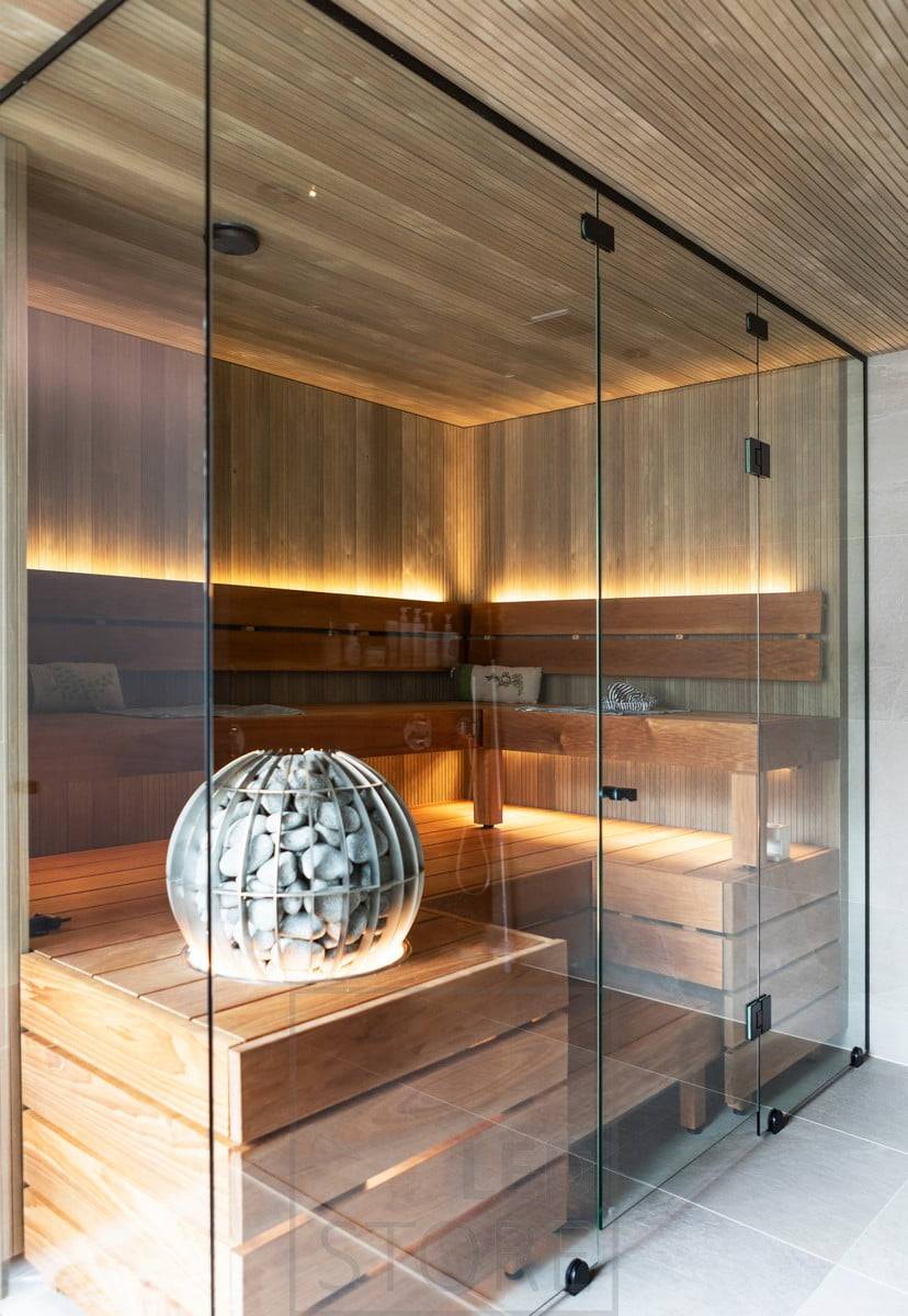 Eine Sauna mit Glaswänden und LED-Lichtband für indirektes Licht hinter der Rückenlehne, unter der Decke und unter dem Ofen.