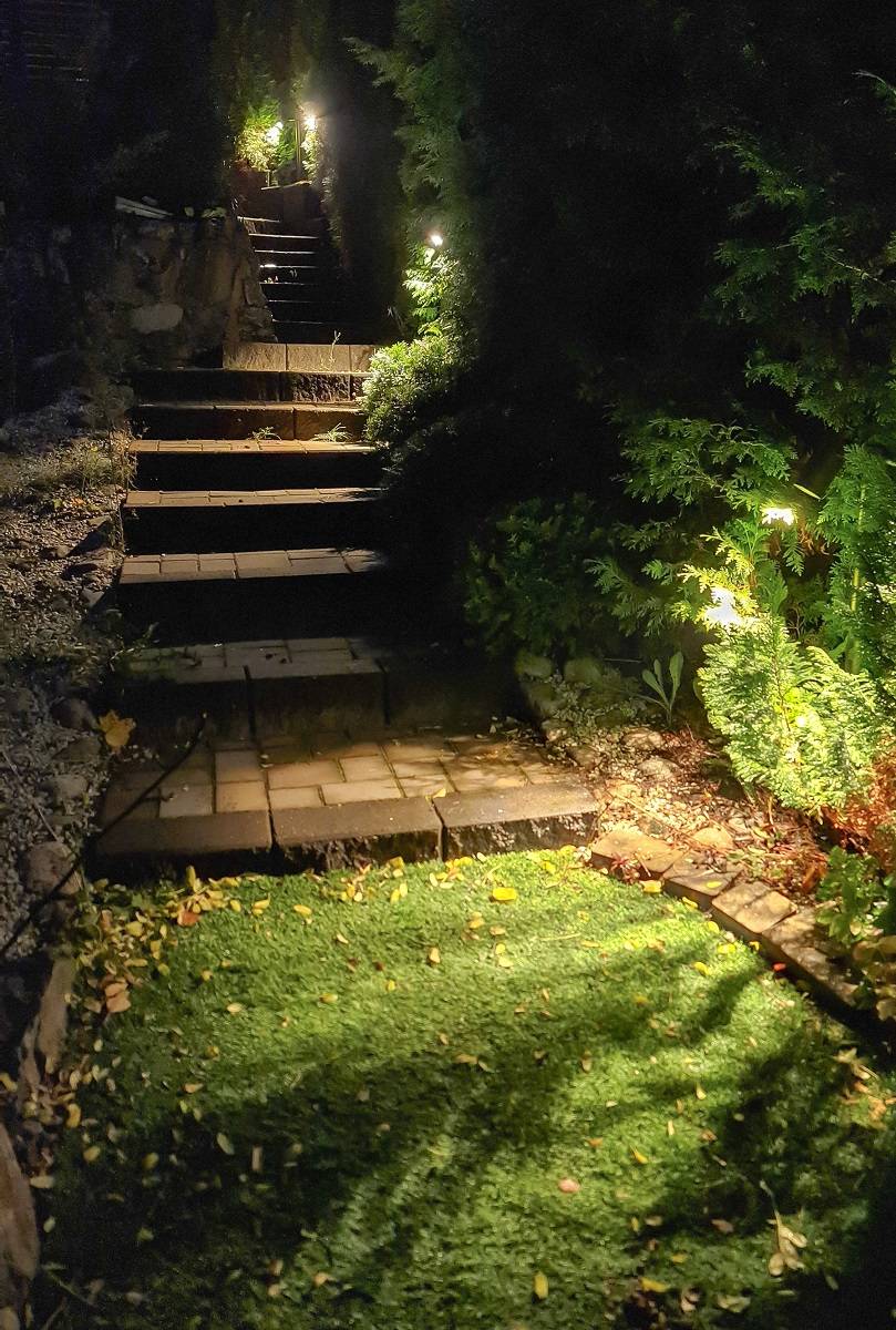TILT 2-Säulenleuchten, die draußen an der Treppe installiert sind. Die Leuchte ist beleuchtet und es dämmert draußen.