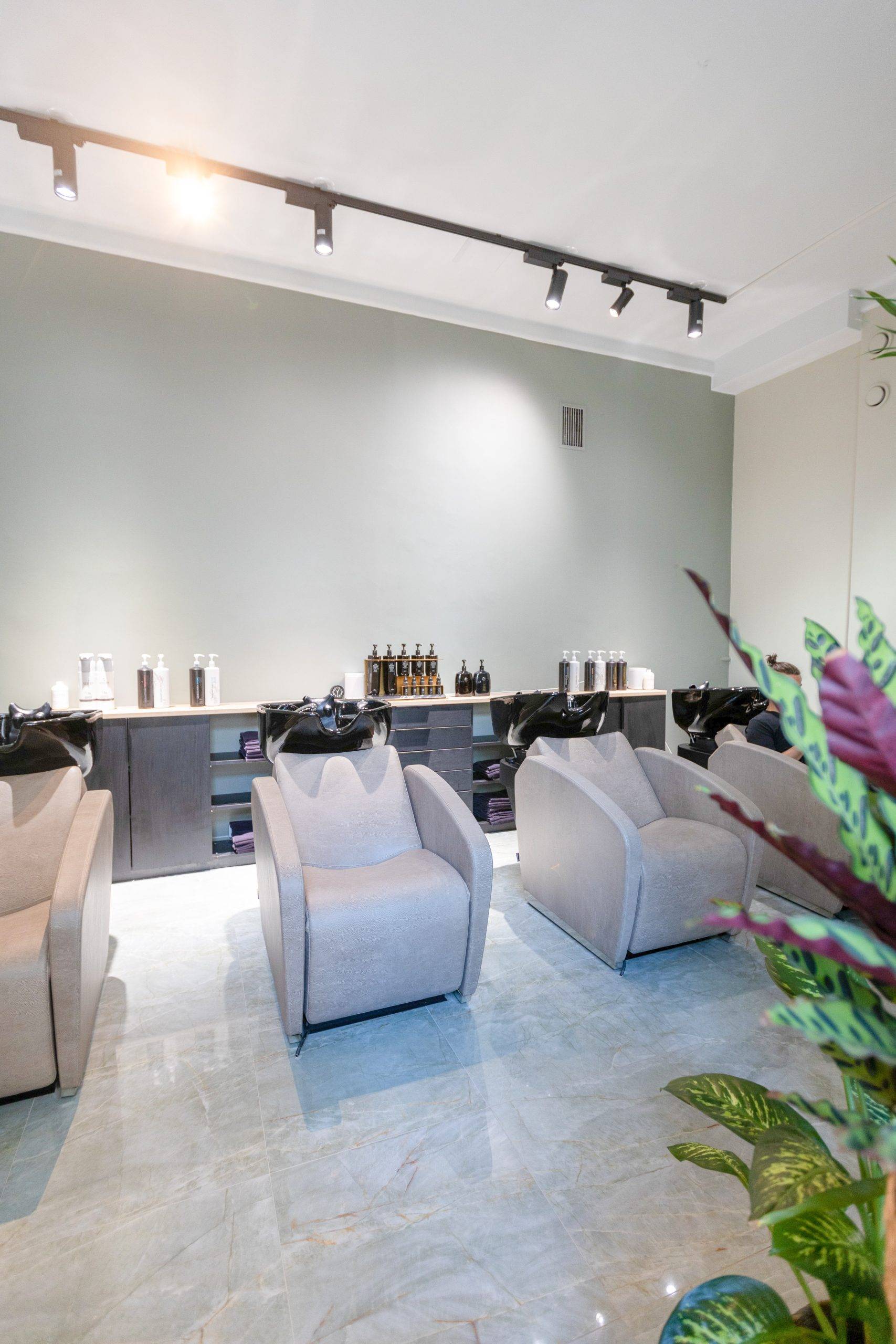 Ein Friseursalon-Waschraum mit hellen Oberflächen und an der Decke montierten schwarzen Drehstromschienen und schwarzen FOKUS-Schienentöpfen.