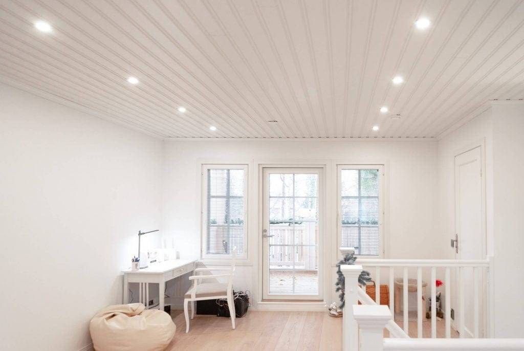 Modernes Zimmer mit LED-Einbauleuchten, weißen Wänden, Schreibtisch, Stuhl, Sitzsack, Glastüren zum Balkon; Treppengeländer auf der rechten Seite.