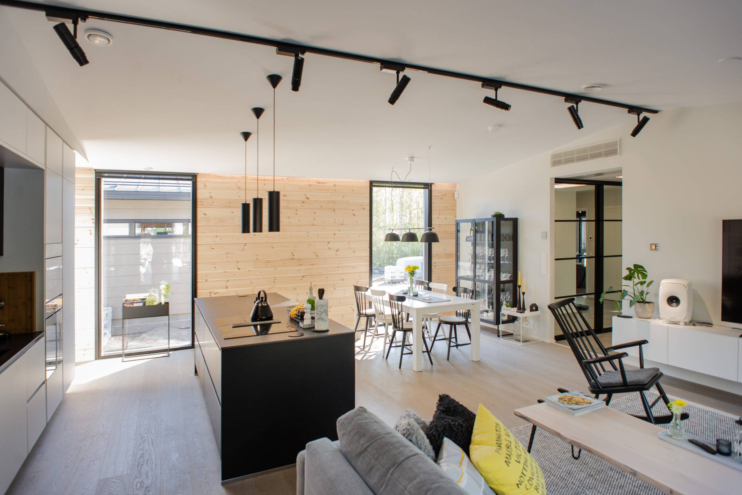 Moderne, offene Küche und Wohnzimmer mit Holzdetails und schwarzen Möbeln für einen stilvollen Look. Die hochwertige Innenbeleuchtung von LedStore.fi schafft eine tolle Atmosphäre, und die großen Fenster lassen natürliches Licht herein. 