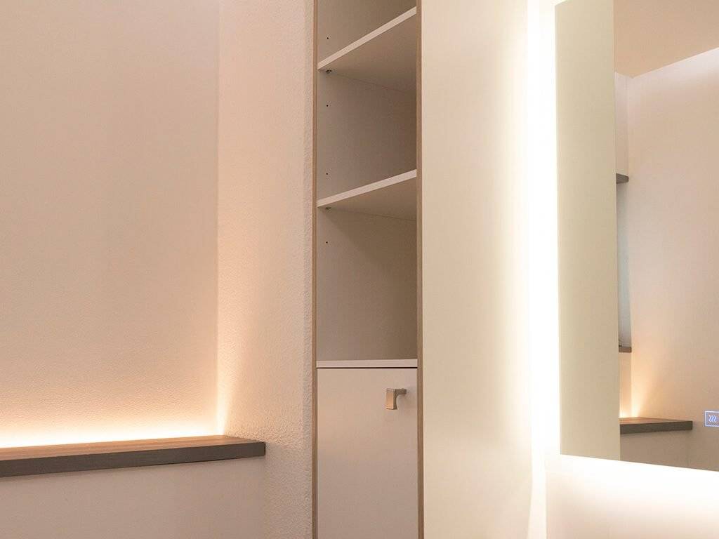 Minimalistisches Dekor, moderne LED-beleuchtete Regale, verspiegelte Wand, sanfte Beleuchtung. Neutrale Farben und klare Linien schaffen einen eleganten und stilvollen Raum.