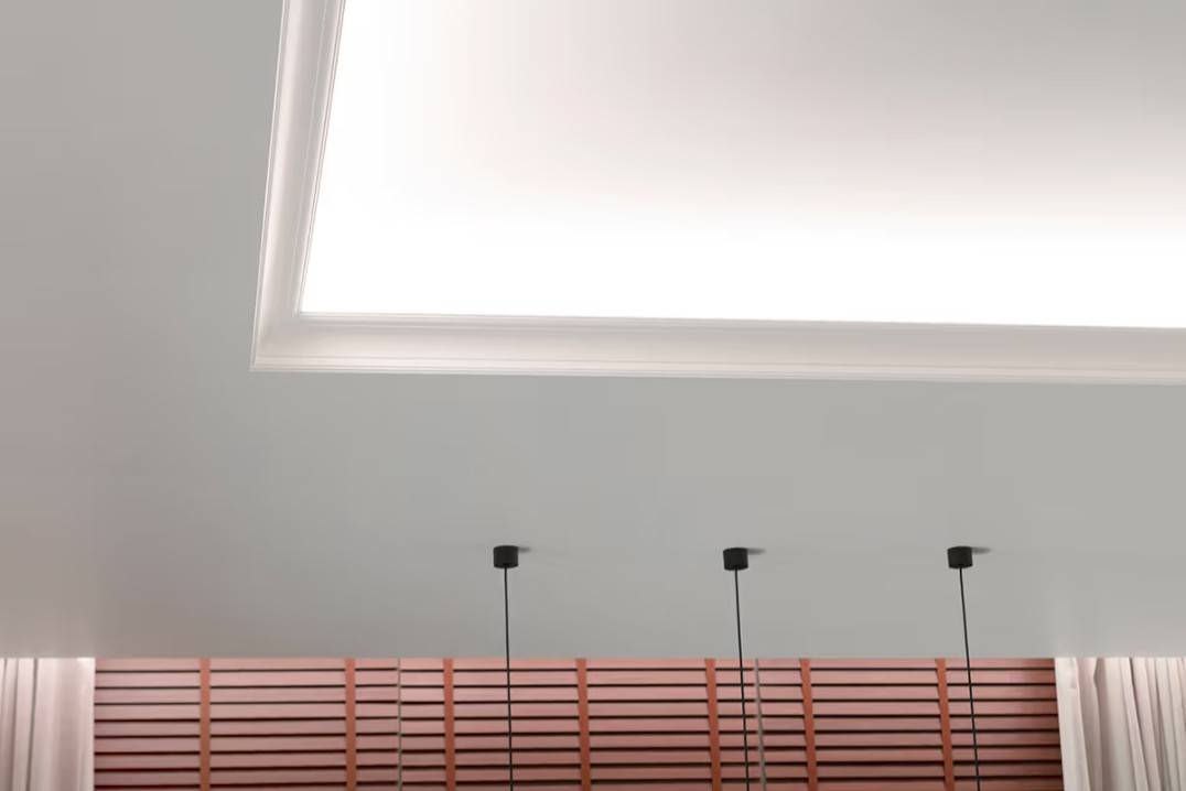 Ein funktionelles Beleuchtungspaket für das Wohnzimmer. Die LED-Leuchtstreifen an der Deckenleuchte leuchten zur Decke und nach unten zu den Vorhängen hin. 