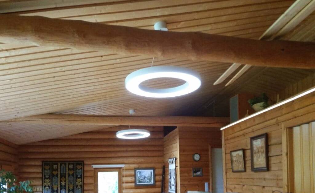 Ein hölzernes Interieur mit kreisrunden LED-Deckenleuchten sorgt für ein warmes Licht. Wände und Decken aus Holz sorgen mit gerahmter Kunst, einer Uhr und Wandteppichen für rustikalen Charme.