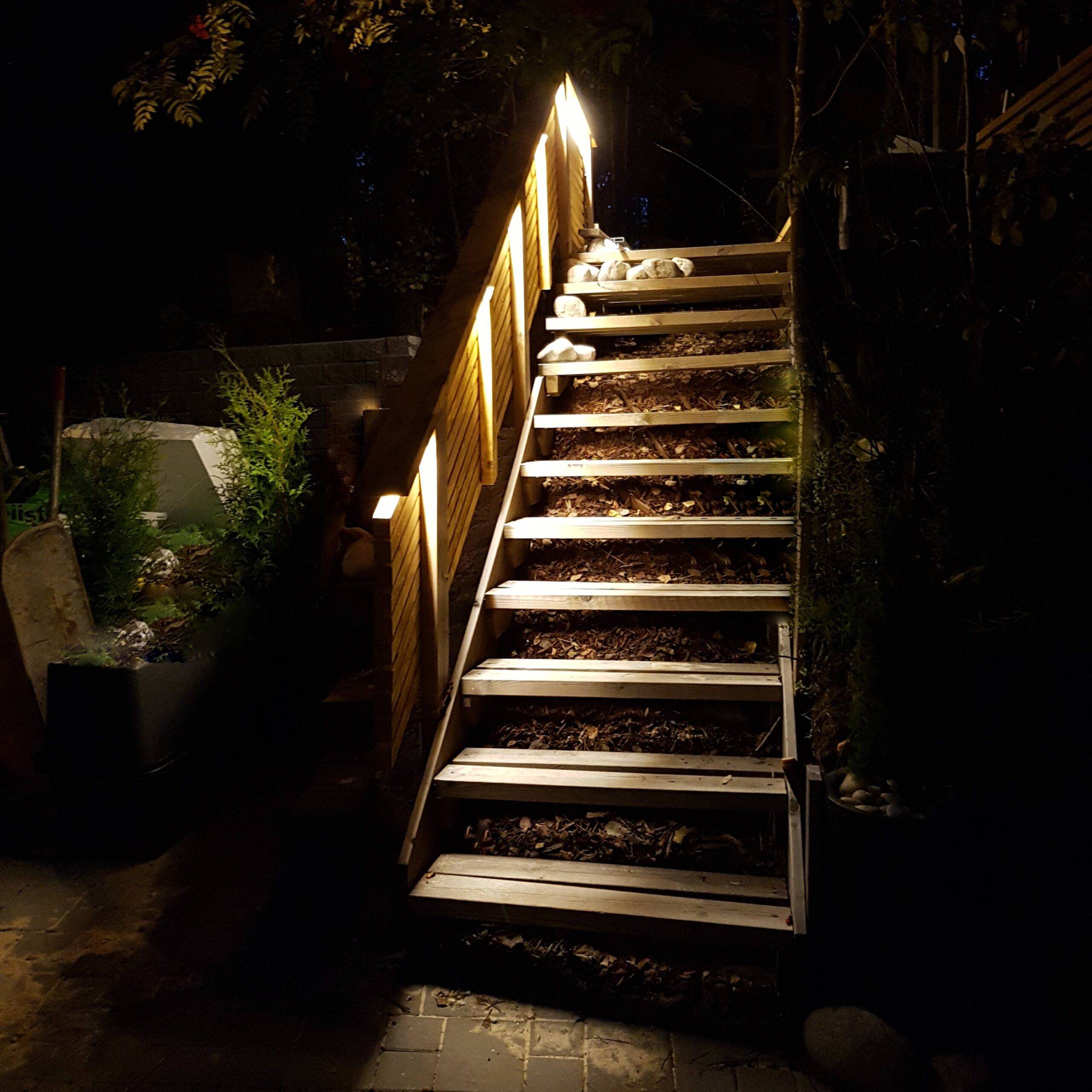 Die Holztreppe im Außenbereich wird von einem warmen LED-Lichtband in einem Aluminiumprofil beleuchtet.