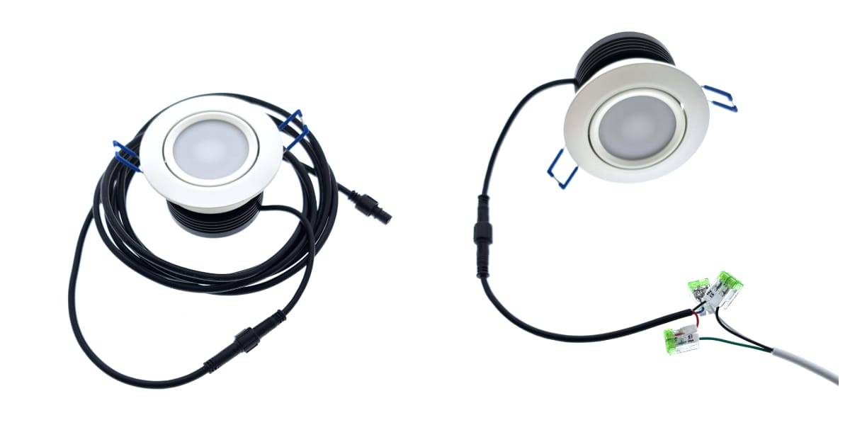 Zwei runde LED-Downlights mit weißem Rahmen sind an langen schwarzen Drähten befestigt. Die Leuchten haben Anschlüsse an den Enden der Drähte. Ein Kabel ist verdrillt, während das andere verlängert und mit den grünen Inline-Steckern verbunden ist, wodurch seine eigene stilvolle LED-Integration hervorgehoben wird.
