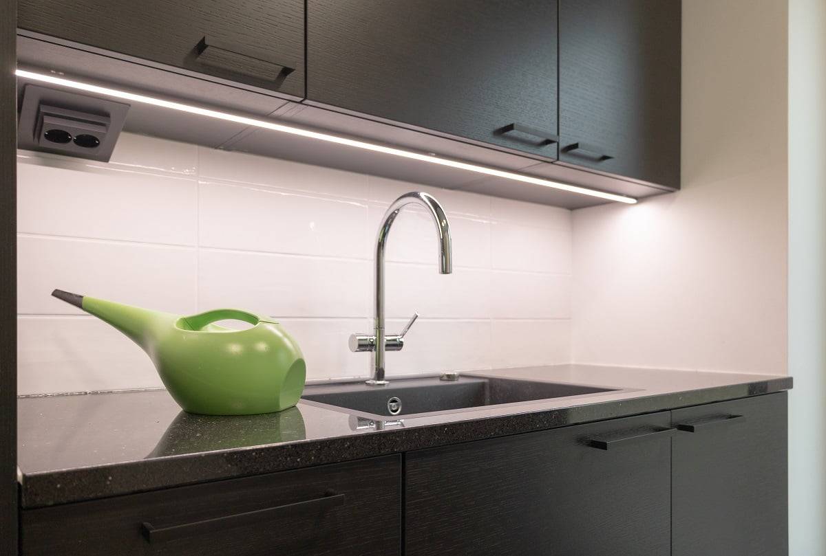 Auf der Arbeitsplatte im Hauswirtschaftsraum wird die dunkle Oberfläche von einer LED-Leiste in einem schwarzen Aluminiumprofil beleuchtet. ©LedStore