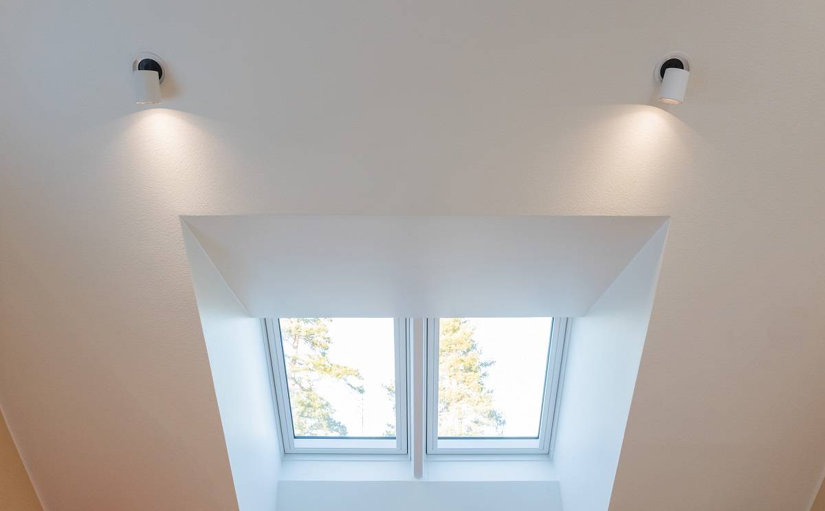 Die weiße Decke ist mit zwei LED-Doppellampen ausgestattet, die die Dachlaterne hell beleuchten. Zwei rechteckige Fenster öffnen sich zur Dachlaterne und geben den Blick auf den blauen Himmel und die Baumkronen frei. Dieses atemberaubende Beleuchtungsset ist bei LedStore.fi erhältlich, wo eine große Auswahl an hochwertigen LED-Lampen auf Sie wartet, um die perfekte Atmosphäre in Ihrem Zuhause zu schaffen.