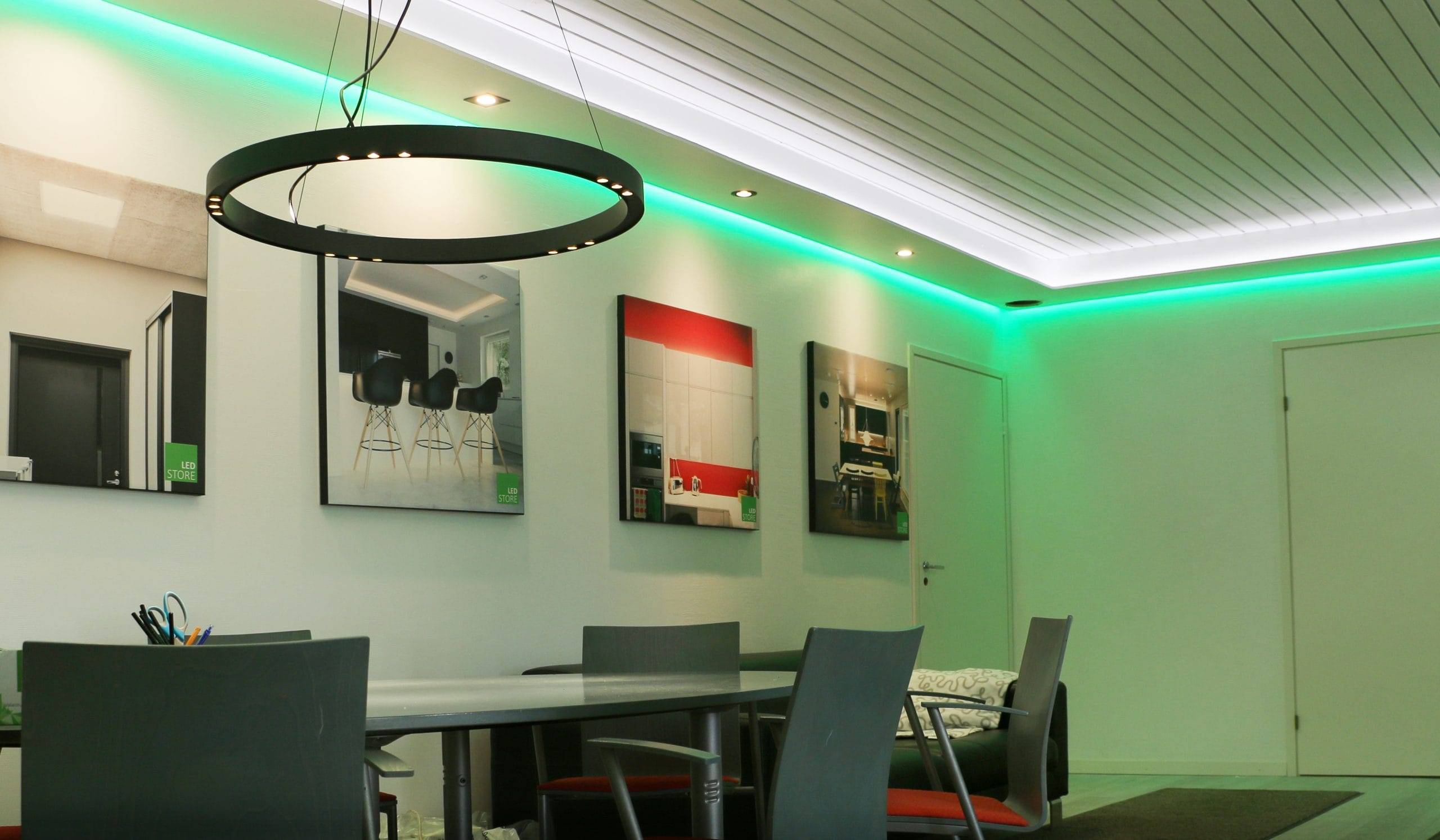 Zigbee-Beleuchtungssteuerung Teil 2 - Überprüfung der Zigbee-Geräte und Kopplung Ein moderner Raum mit einer schwarzen, runden LED-Leuchte, grauen Stühlen um einen langen Tisch, gerahmter Kunst an der Wand und einer Deckenbeleuchtung mit grünen Highlights, die eine elegante Atmosphäre schafft.