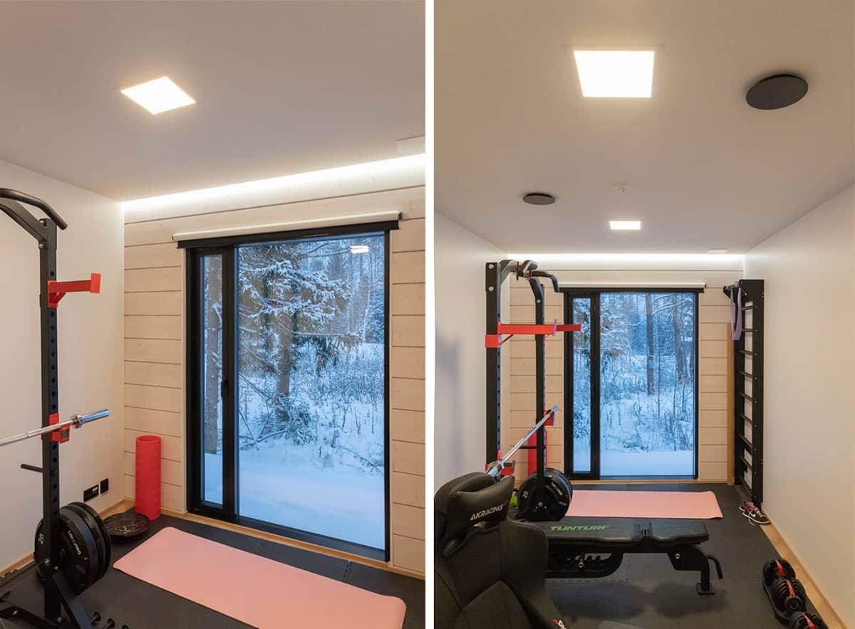 Ein kleiner Fitnessraum mit einem großen Fenster nach draußen, zwei kleinen Paneel-Leuchten an der Decke und einer LED-Leiste über dem Fenster.