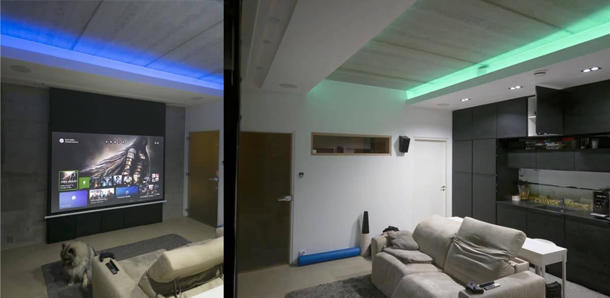 Modernes Wohnzimmer mit LedStore.fi LED-Beleuchtung für das Heimkino, Projektorleinwand, bequemen Sitzgelegenheiten und einem Hund auf dem Boden.