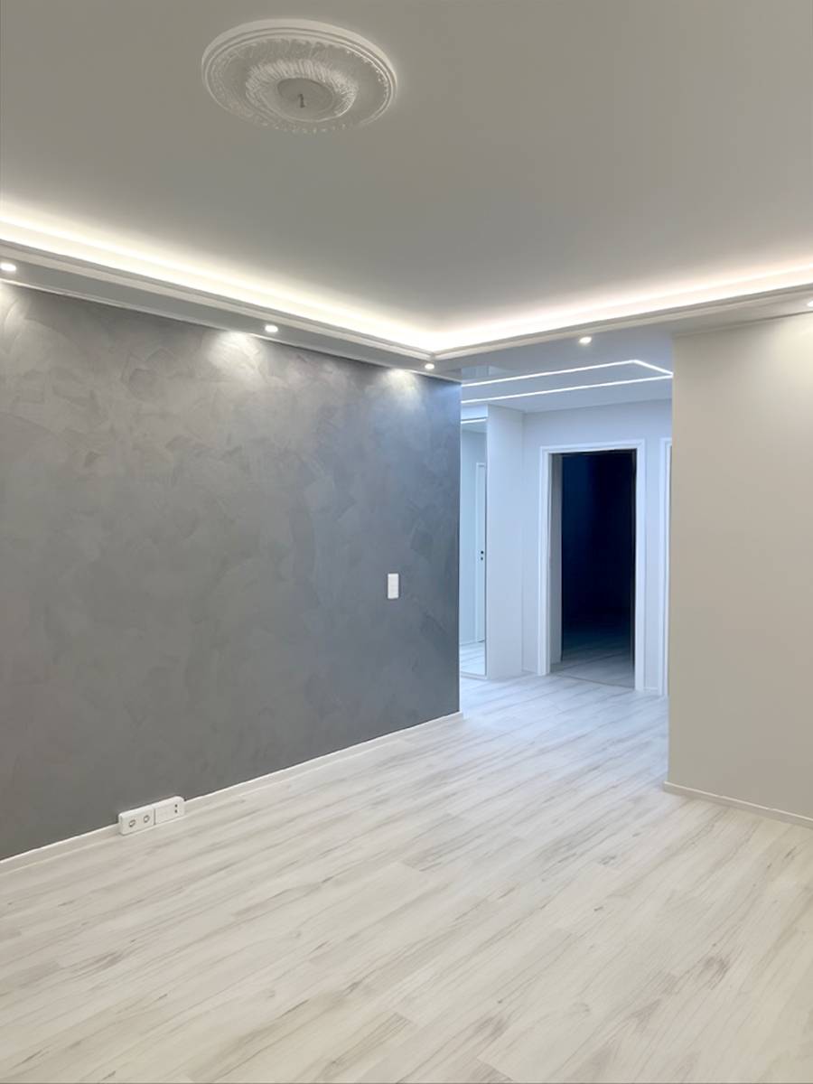 Eine Deckenkonstruktion mit abgehängter Decke an den Raumkanten, mit indirekter LED-Beleuchtung und nach unten gerichteten Strahlern.