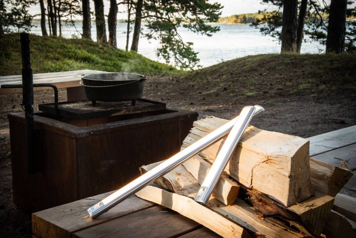 Zwei WANDA-Lampen unterschiedlicher Länge lehnen draußen an Holzstämmen.